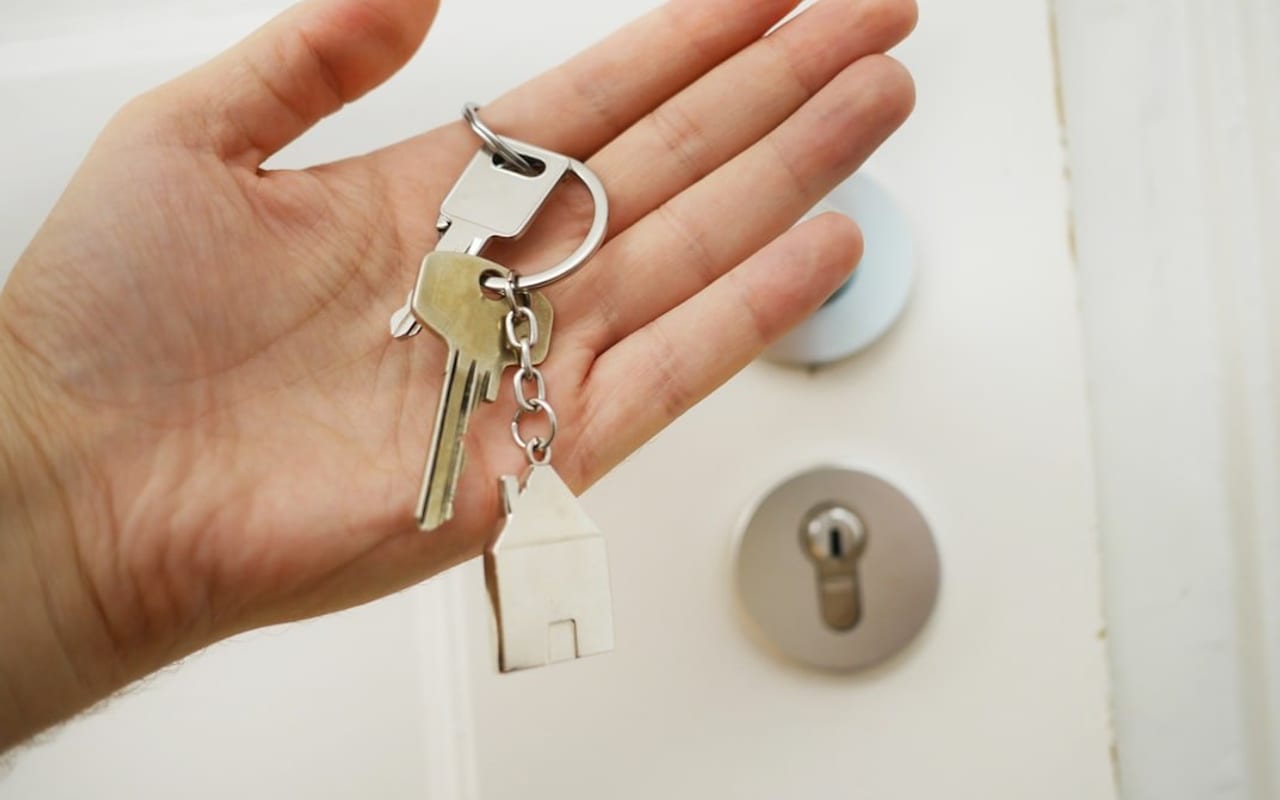 A hand holding a house-shaped keychain in front of a white door