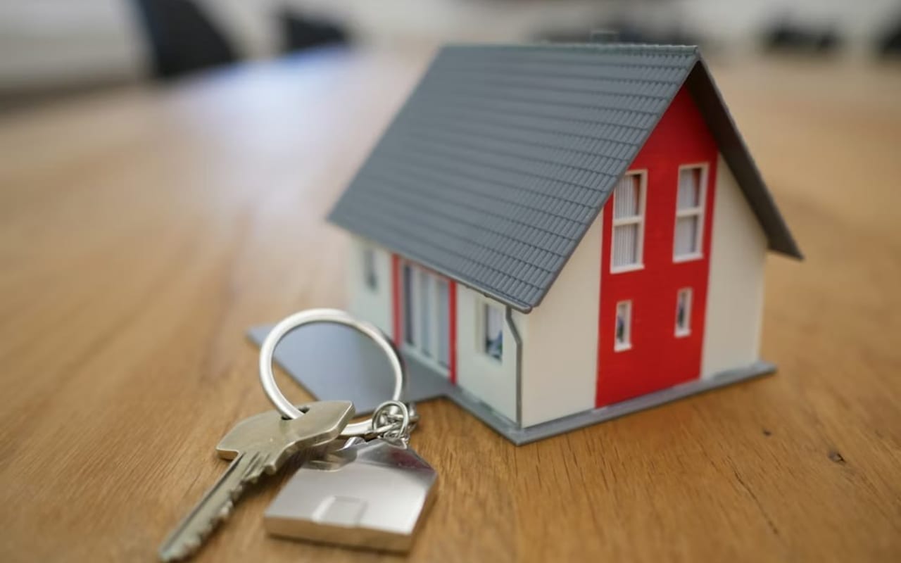 A small model house and a set of keys resting on a wooden surface